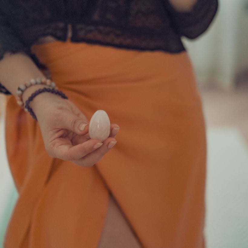 femme tiens un oeuf de yoni en quartz rose devant son perinee